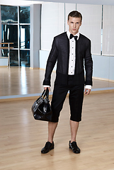 Image showing Male fashion, beauty concept. Elegant young fashion man holds in his hand a black bag and looking to the camera. Classic style. Studio shot