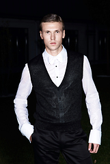 Image showing Male fashion, beauty concept. Portrait of young man with short wet hair wearing black suit, posing on street. Classic style.