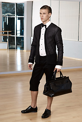 Image showing Male fashion, beauty concept. Elegant young fashion man holds in his hand a black bag and looking to away from the camera. Classic style. Studio shot