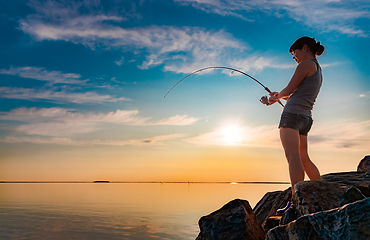 Image showing Woman fishing on Fishing rod spinning at sunset background.