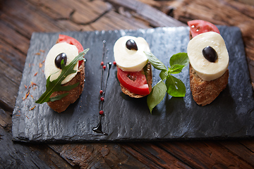 Image showing Italian bruschetta with chopped tomatoes, basil, mozzarella cheese and balsamic vinegar. Fresh homemade caprese bruschetta or crostini over black stone background, copy space.