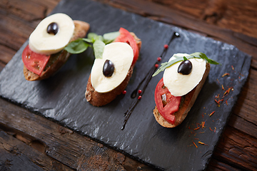 Image showing Italian bruschetta with chopped tomatoes, basil, mozzarella cheese and balsamic vinegar. Fresh homemade caprese bruschetta or crostini over black stone background, copy space.