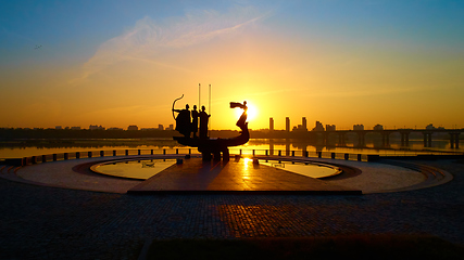 Image showing Monument to the founders of Kyiv at sunrise, wide-angle view with blue sky and yellow sun. Statue of Kyi, Shchek, Horyv and Lybid.