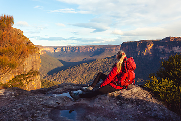 Image showing Woman sits at cliff edge and takes in magnificent mountain views