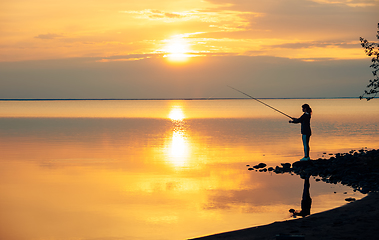 Image showing Woman fishing on Fishing rod spinning at sunset background.