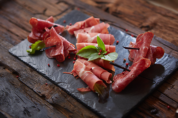 Image showing Slices of Italian prosciutto crudo or jamon with fresh basil leaves on a black background.