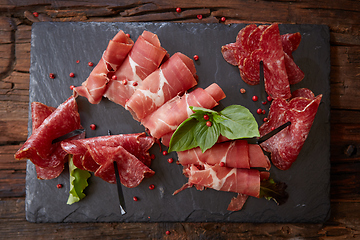 Image showing Slices of Italian prosciutto crudo or jamon with fresh basil leaves on a black background.