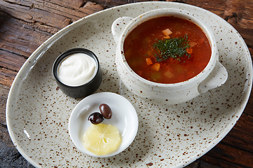 Image showing Soup saltwort with lemon, meat, pickles, tomato sauce olives in a bowl on a sacking.