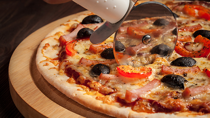 Image showing Pizza cutter wheel slicing ham pizza