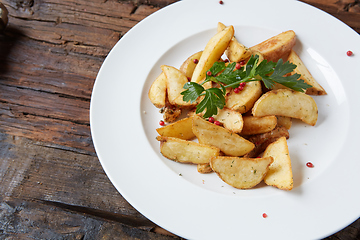 Image showing Homemade roasted potato with parsley on rustic background.