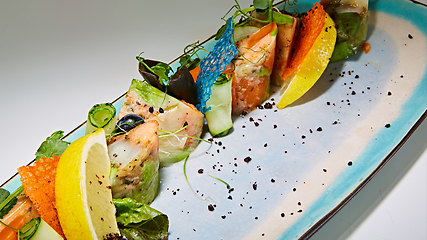 Image showing fried fish rolls with herbs and vegetables on blue plate.