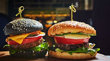 Image showing Set of homemade burgers in black and white buns with tomato, lettuce, cheese, onion on wood serving board over dark table. Rustic style. Homemade fast food.