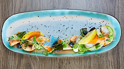 Image showing fried fish rolls with herbs and vegetables on blue plate.