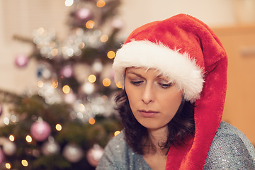 Image showing Beautiful middle age woman in santa hat sitting near the Christmas tree