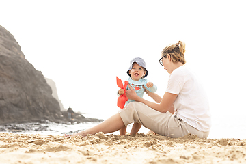 Image showing Mother playing his infant baby boy son on sandy beach enjoying summer vacationson on Lanzarote island, Spain. Family travel and vacations concept.