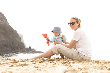 Image showing Mother playing his infant baby boy son on sandy beach enjoying summer vacationson on Lanzarote island, Spain. Family travel and vacations concept.