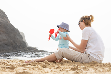 Image showing Mother playing his infant baby boy son on sandy beach enjoying summer vacationson on Lanzarote island, Spain. Family travel and vacations concept.