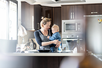 Image showing Happy mother and little infant baby boy making pancakes for breakfast together in domestic kitchen. Family, lifestyle, domestic life, food, healthy eating and people concept.