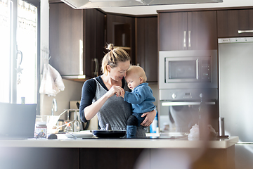 Image showing Happy mother and little infant baby boy making pancakes for breakfast together in domestic kitchen. Family, lifestyle, domestic life, food, healthy eating and people concept.