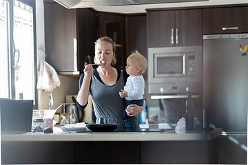 Image showing Happy mother and little infant baby boy prepering healthy breakfast together in domestic kitchen. Family, lifestyle, domestic life, food, healthy eating and people concept.