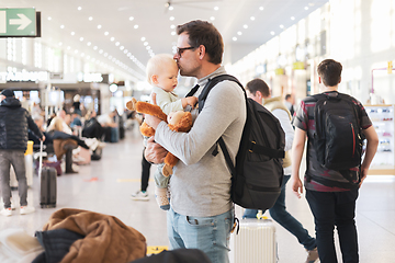 Image showing Father traveling with child, holding and kising his infant baby boy at airport terminal waiting to board a plane. Travel with kids concept.