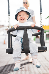 Image showing Mother pushing her infant baby boy child on a swing on playground outdoors.