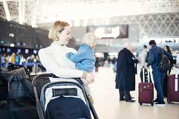 Image showing Motherat travelling with his infant baby boy child, walking, pushing baby stroller and luggage cart at airport terminal station. Travel with child concept.