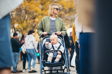 Image showing Mother waling and pushing his infant baby boy child in stroller in crowd of people wisiting sunday flea market in Malaga, Spain.