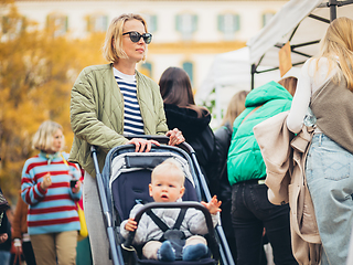 Image showing Mother waling and pushing his infant baby boy child in stroller in crowd of people wisiting sunday flea market in Malaga, Spain.