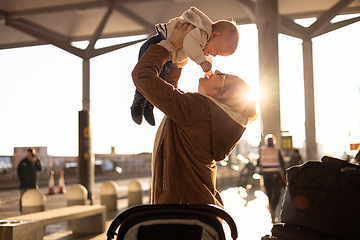 Image showing Motherat happily holding and lifting his infant baby boy child in the air after being rejunited in front of airport terminal station. Baby travel concept.