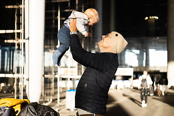 Image showing Father happily holding and lifting his infant baby boy child in the air after being rejunited in front of airport terminal station. Baby travel concept.