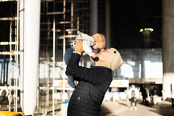 Image showing Father happily holding and lifting his infant baby boy child in the air after being rejunited in front of airport terminal station. Baby travel concept.