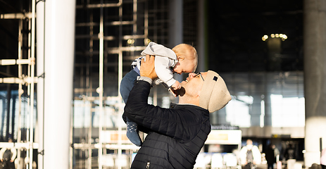 Image showing Father happily holding and lifting his infant baby boy child in the air after being rejunited in front of airport terminal station. Baby travel concept.