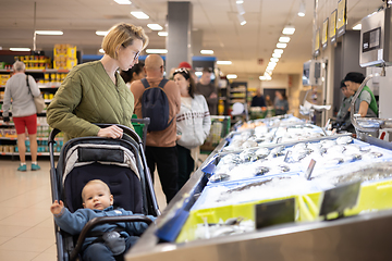 Image showing Casualy dressed mother choosing fish in the fish market department of supermarket grocery store with her infant baby boy child in stroller.