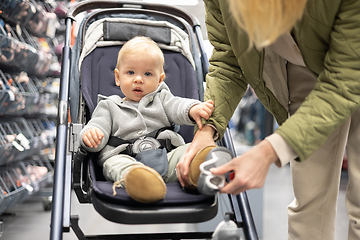 Image showing Casualy dressed mother choosing sporty shoes and clothes products in sports department of supermarket store with her infant baby boy child in stroller.