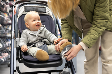 Image showing Casualy dressed mother choosing sporty shoes and clothes products in sports department of supermarket store with her infant baby boy child in stroller.