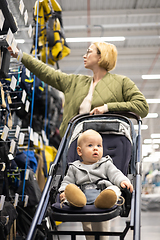 Image showing Casualy dressed mother choosing sporty shoes and clothes products in sports department of supermarket store with her infant baby boy child in stroller.