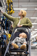 Image showing Casualy dressed mother choosing sporty shoes and clothes products in sports department of supermarket store with her infant baby boy child in stroller.