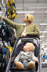 Image showing Casualy dressed mother choosing sporty shoes and clothes products in sports department of supermarket store with her infant baby boy child in stroller.