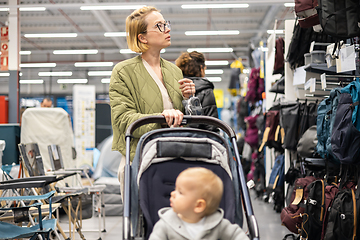 Image showing Casualy dressed mother choosing sporty shoes and clothes products in sports department of supermarket store with her infant baby boy child in stroller.