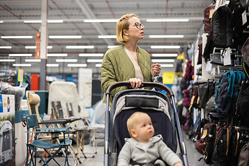 Image showing Casualy dressed mother choosing sporty shoes and clothes products in sports department of supermarket store with her infant baby boy child in stroller.