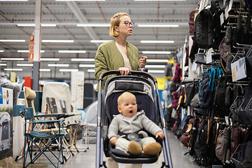 Image showing Casualy dressed mother choosing sporty shoes and clothes products in sports department of supermarket store with her infant baby boy child in stroller.