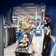 Image showing Casualy dressed mother choosing sporty shoes and clothes products in sports department of supermarket store with her infant baby boy child in stroller.