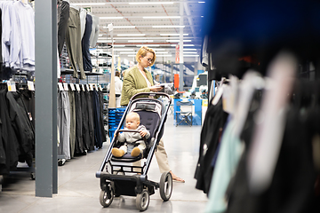 Image showing Casualy dressed mother choosing sporty shoes and clothes products in sports department of supermarket store with her infant baby boy child in stroller.