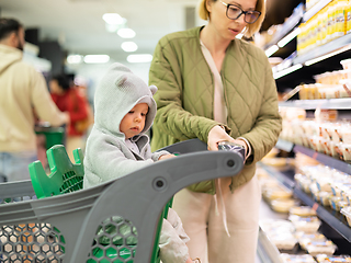 Image showing Casualy dressed mother choosing products in department of supermarket grocery store with her infant baby boy child in shopping cart.