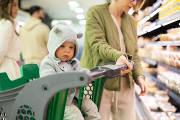 Image showing Casualy dressed mother choosing products in department of supermarket grocery store with her infant baby boy child in shopping cart.