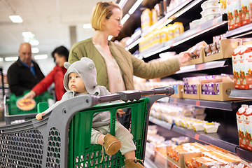 Image showing Casualy dressed mother choosing products in department of supermarket grocery store with her infant baby boy child in shopping cart.