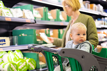 Image showing Casualy dressed mother choosing products in department of supermarket grocery store with her infant baby boy child in shopping cart.