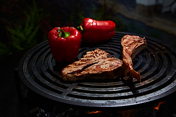 Image showing Tomahawk rib beef steak and T-bone on hot black grill.