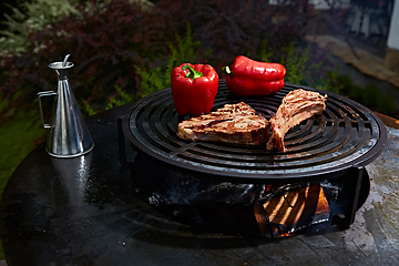 Image showing Tomahawk rib beef steak and T-bone on hot black grill.